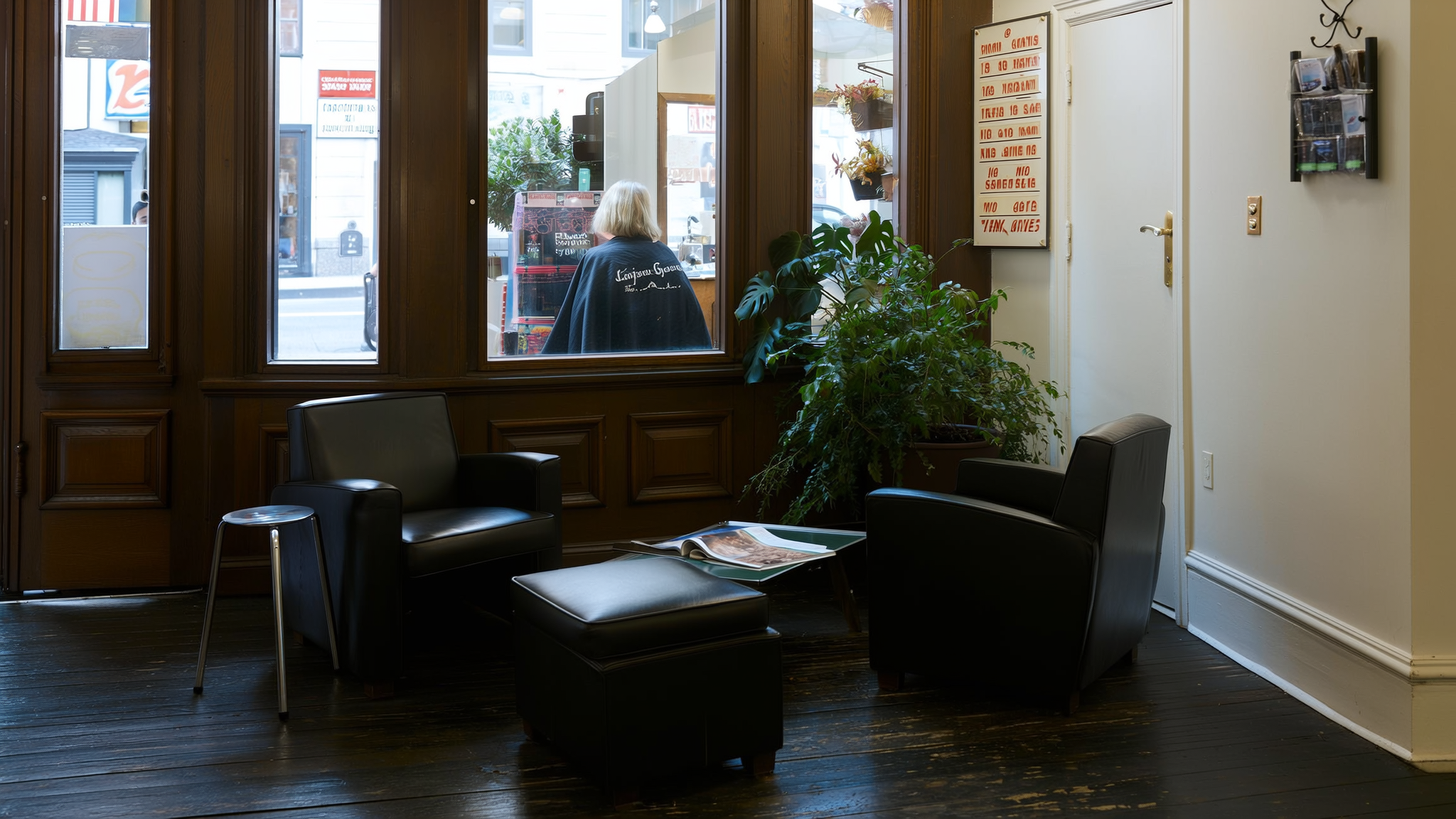 De wachthoek bij het raam, met een leren fauteuil, een lage tafel en een grote plant.